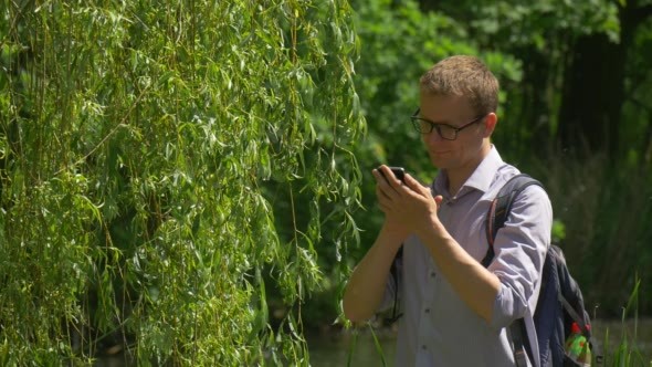 Man in Glasses Clicks a Phone in Park Walking
