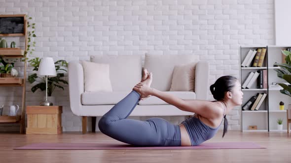 Asian woman practicing yoga pose Bow at home.