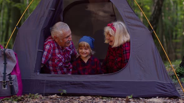 Senior Grandmother Grandfather with Granddaughter Sitting in Tourist Tent Over Campfire in Wood