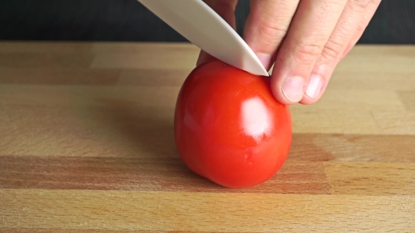 Man Splitting Ripe Red Tomato With White Knife