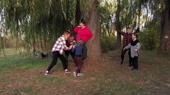 Group of Friendly Active People with Children and Grandmother Ride Swing in Summer Park Play