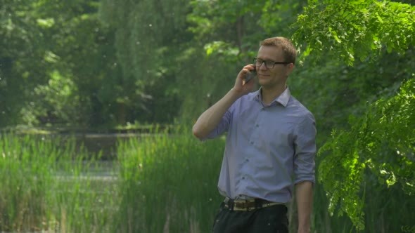 Man Types a Number Talking on Smartphone in Park