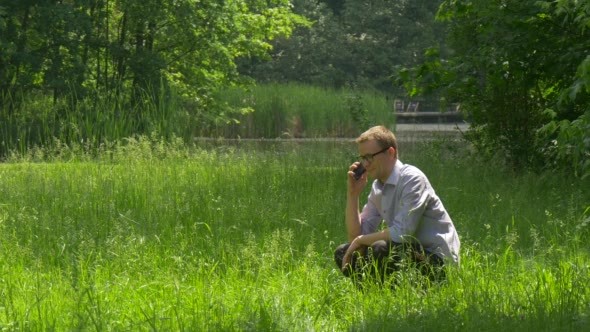 Man Talking by Phone Sits to a Ground Green Park