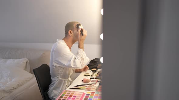 Side View Portrait Travesty WomanSitting at Table with Cosmetics Applying Face Powder in Slow Motion