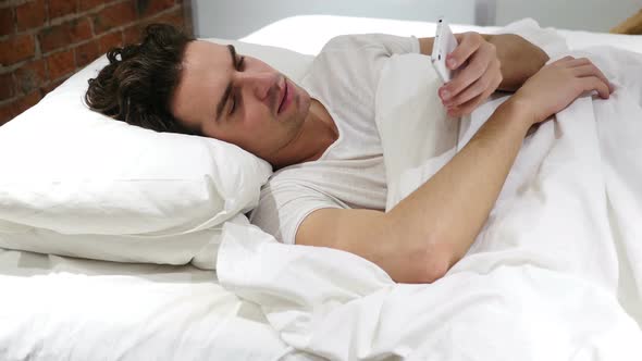 Man in Bed Browsing on Smartphone at Night