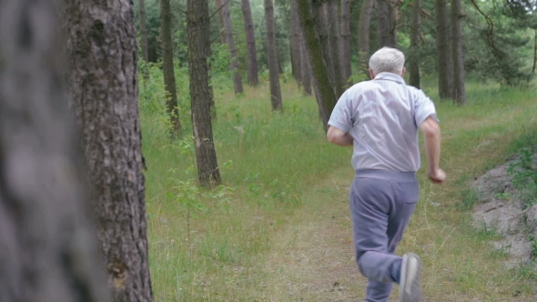 Old Man Running Outdoors In a Coniferous Forest. Camera Behind Him