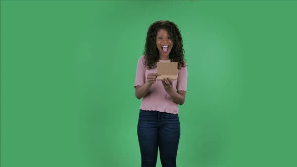 Portrait of Beautiful African American Young Woman Is Looking at Camera and Opening the Gift with a