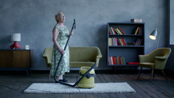 Happy Elderly Woman Dancing With a Vacuum Cleaner