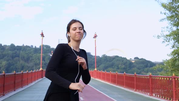 Attractive Brunette Girl Listening To Music and Dancing at Sunrise on the Bridge. A Happy Woman