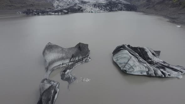 Aerial view over ice blocks on the Solheimajokull glacier lagoon - tilt, drone shot