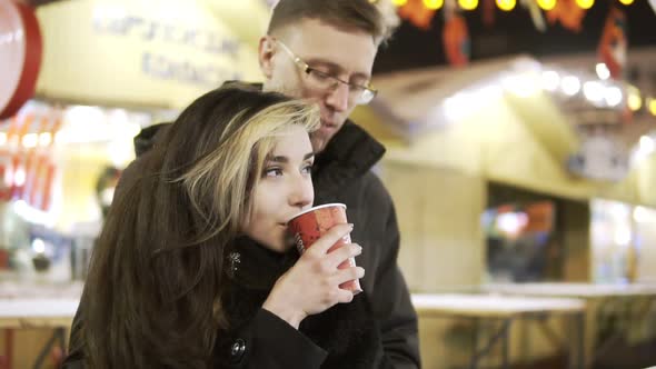 Happy Attractive Couple Drinking Tea in a Christmas Market at Night