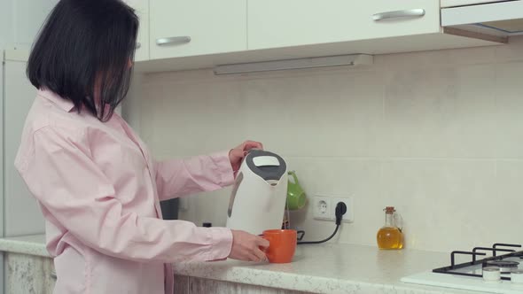 Housewife pouring hot water in teapot to prepare the tea for breakfast in the morning