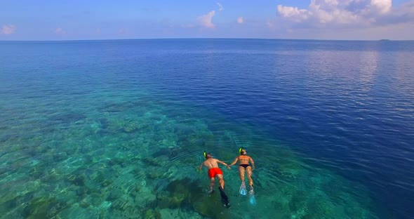 Aerial drone view of a man and woman couple snorkeling over the coral reef of a tropical island.