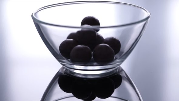 Round Chocolate Candies Falling Down In a Glass Bowl