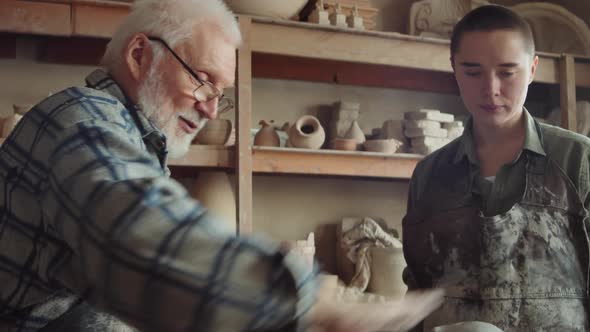 Elderly Sculptor Teaching Young Apprentice in Pottery Studio