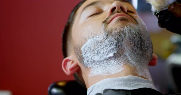 Barber applying shaving cream on client beard 