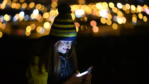 Woman checking phone at night with city lights as background