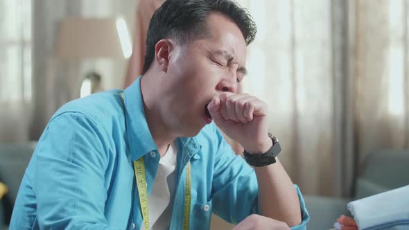 Close Up Of Asian Male Designer Working On A Laptop, Yawning, And Sleeping While Designing Clothes