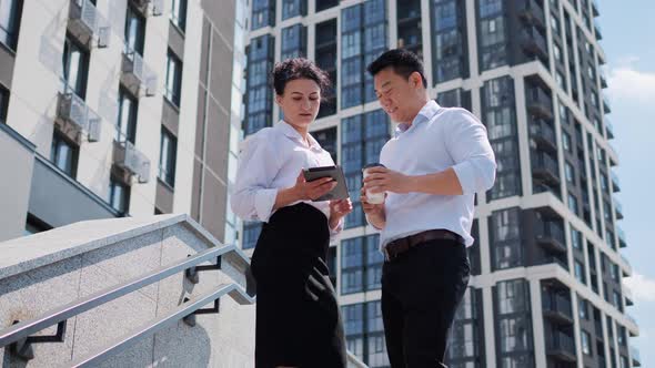 Executive Bank Employees Discuss Report Looking on Tablet on the Stairs