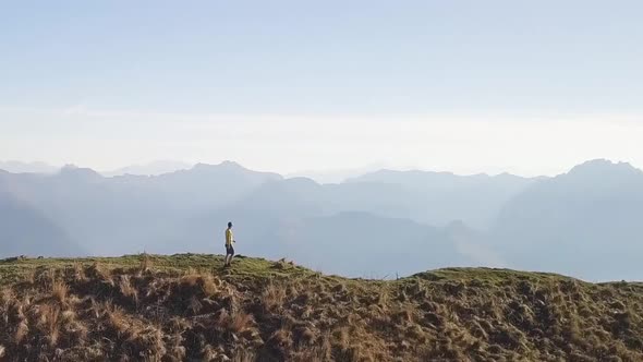 A men walks on a huge mountain ridge. The camera orbits around, the backgroundes very fast.