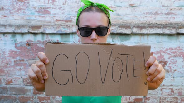 Woman shows cardboard with Go Vote sign brick wall urban background Voting concept Political choice