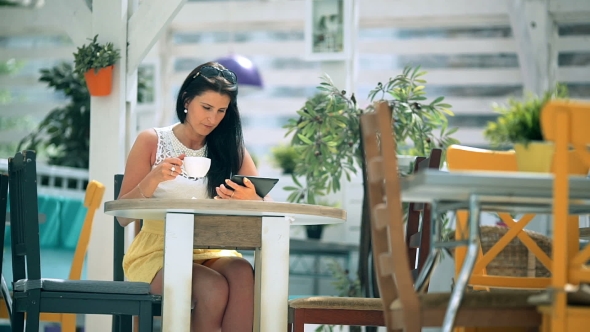 Happy Young Woman Drinking Coffee / Tea And Using Tablet In a Coffee Shop
