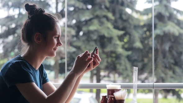 Woman Using Smartphone Sitting Near the Window
