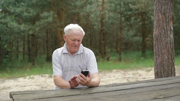 The Old Man Uses The Phone At The Table In The Forest