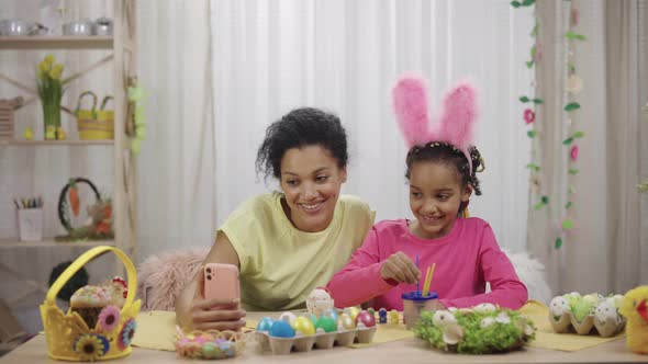 Mom and Daughter with Funny Bunny Ears Talk on a Video Call Using the Phone