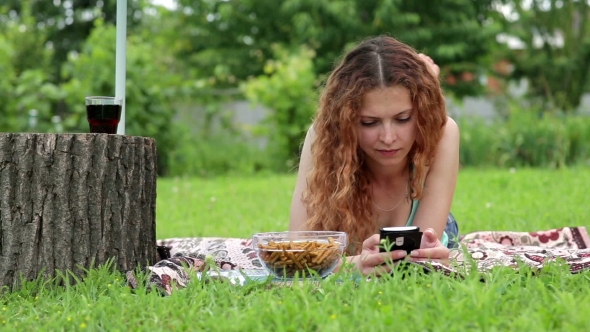 Young Woman Using Mobile Phone And Lying On The Green Grass