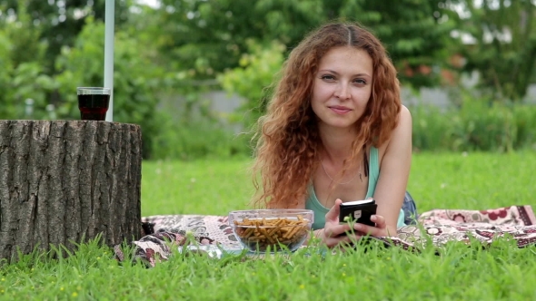 Young Woman Using Mobile Phone And Lying On The Green Grass