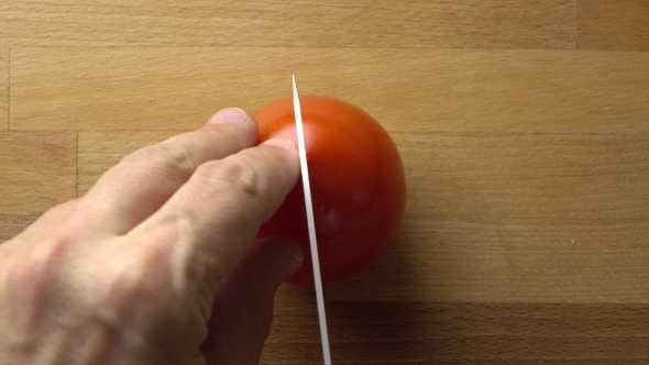 Man Splitting Whole Red Tomato On The Wooden Cutting Board