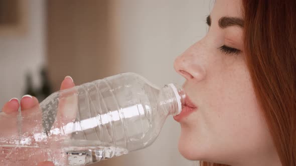 fitness red hair girl drinking from sport bottle during a workout pause at home or gym.