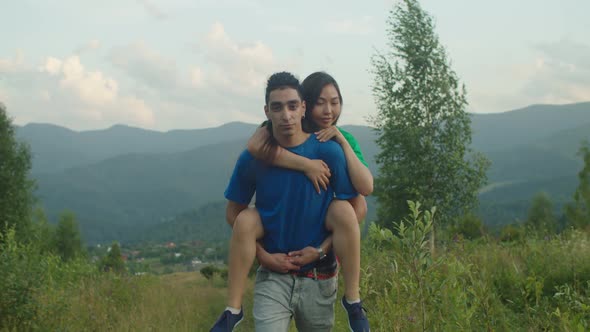 Carefree Arab Man Piggybacking Joyful Excited Asian Girlfriend in Mountains