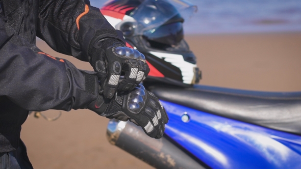 Biker In The Street Next To His Bike, Puts On Gloves. alt