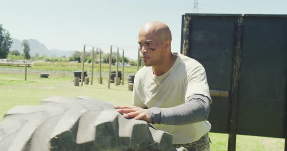 Fit african american male soldier rolling tractor tyre on army obstacle course in the sun