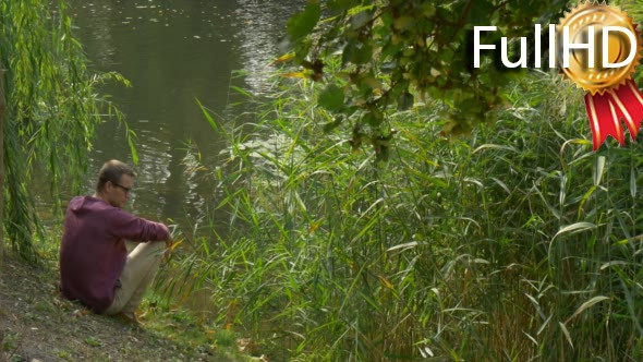 Man is Sitting Close to Water and Lush Green