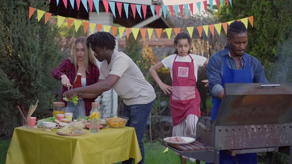 Joyful Teenage Girl Walking in Slow Motion to Busy Group of Multiethnic Friends Cooking Barbecue and