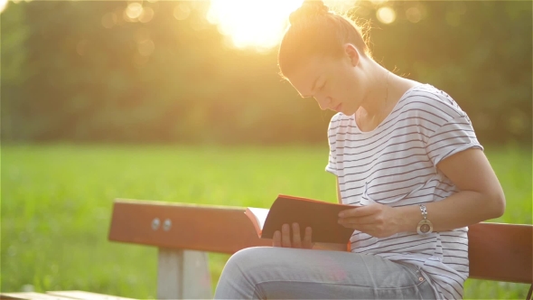 Beautiful Woman Sitting On a Bench In The Park And Reading a Book, Student Preparing For The Exam In