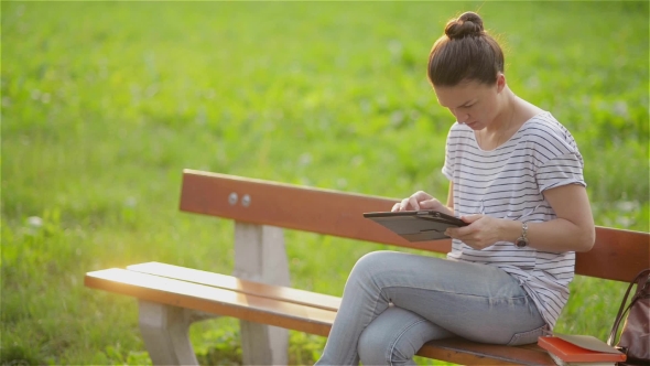 Cute Young Woman With Tablet In The Park, Beautiful Woman Using a Tablet On a Bench In The Garden