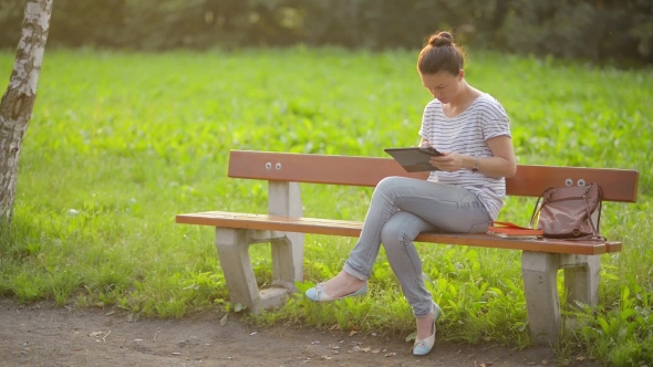 Cute Young Woman With Tablet In The Park, Beautiful Woman Using a Tablet On a Bench In The Garden