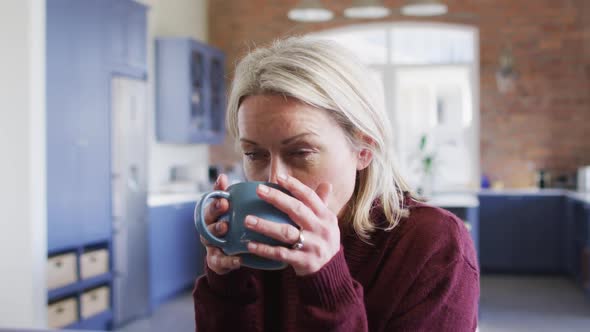 Thoughtful senior caucasian woman in living room sitting on sofa, drinking coffee