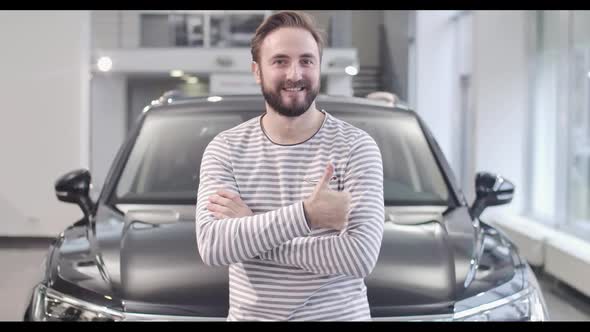 Portrait of Smiling Caucasian Man in Stripped Sweater Showing Thumb Up in Front of New Car