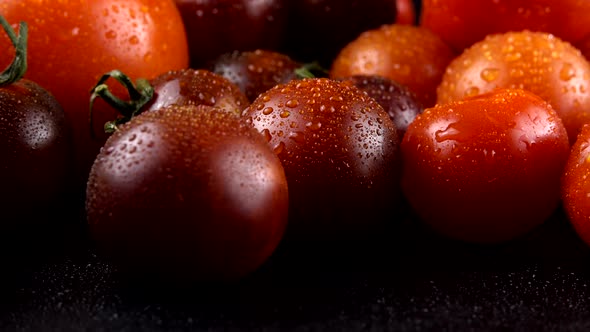 Cherry tomatoes on a black background in water drops.