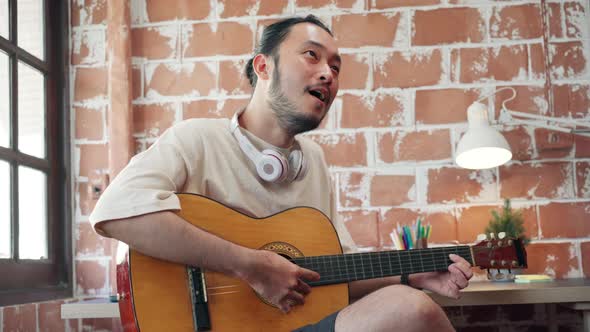 Artists producing music in their home sound studio, Asian man playing guitar and singing.