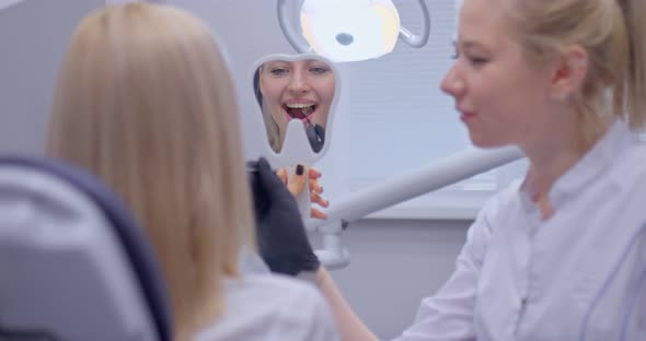 Nice Girl Patient Is Looking at How Her Tooth Was Filled in the Mirror. Satisfied Patient Looks in