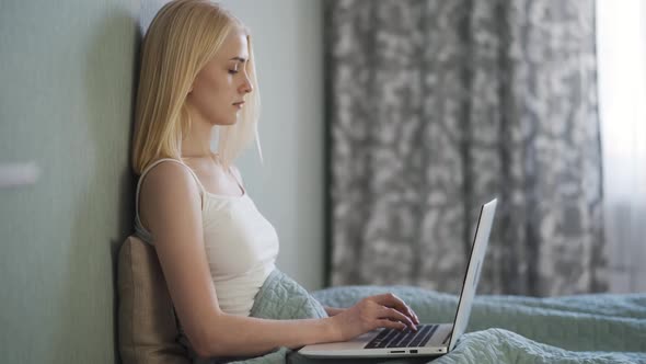 Smiling Young Woman Sitting on Couch Using Laptop Notebook Looking at Screen Typing Message