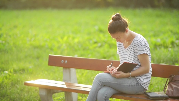 Beautiful Young Woman Is Writing a Diary Outdoors In The Park