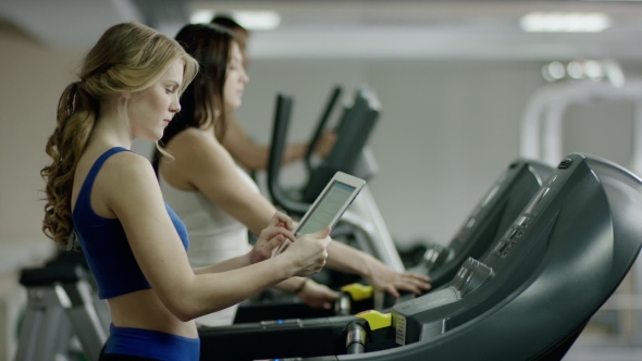 Pretty Woman Walking On Treadmill With The Tablet