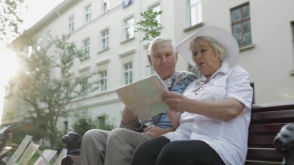 Senior Tourists Sitting on Bench with a Map in Hands Looking for Route